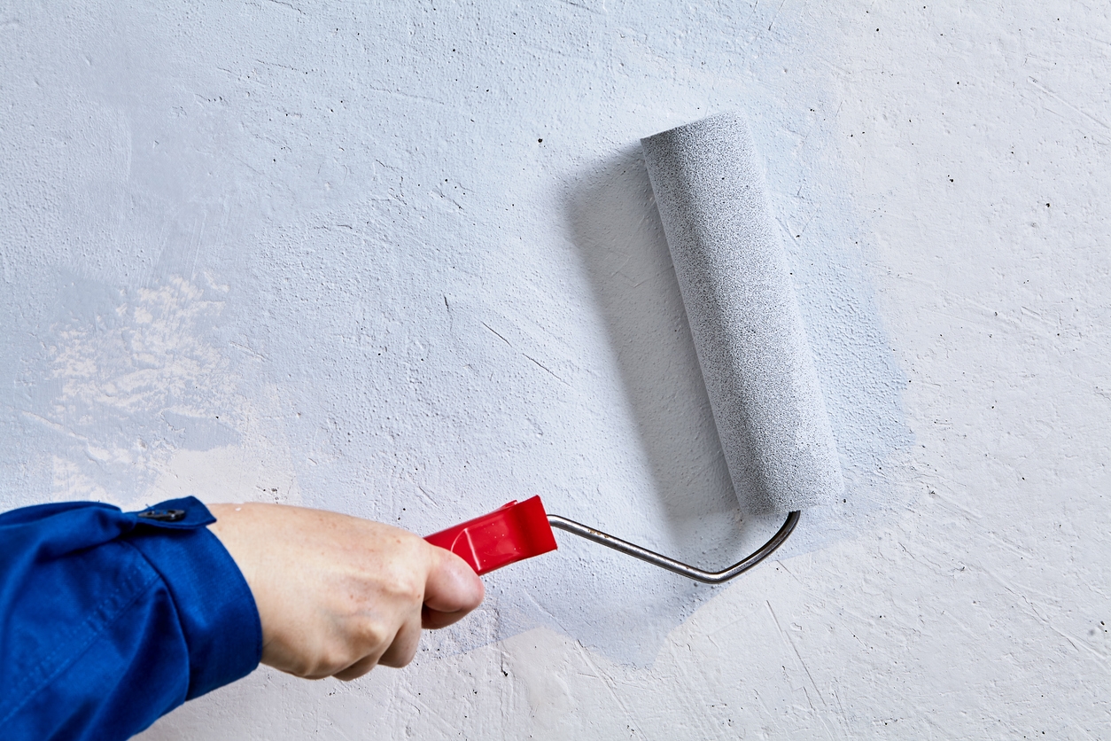 Handyman is painting wall with help of paint roller during home repair.