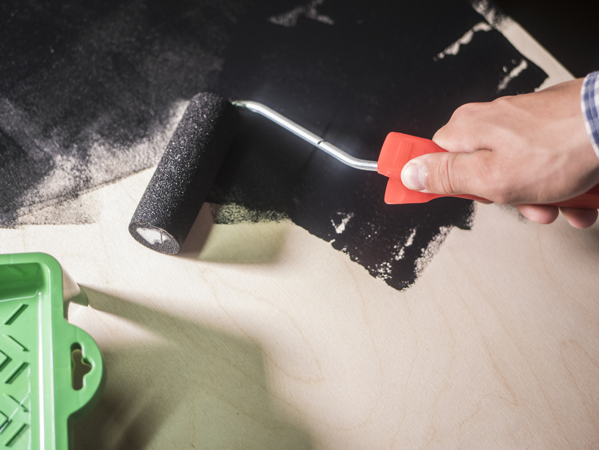 hand painting the wooden surface with black color using roller painter